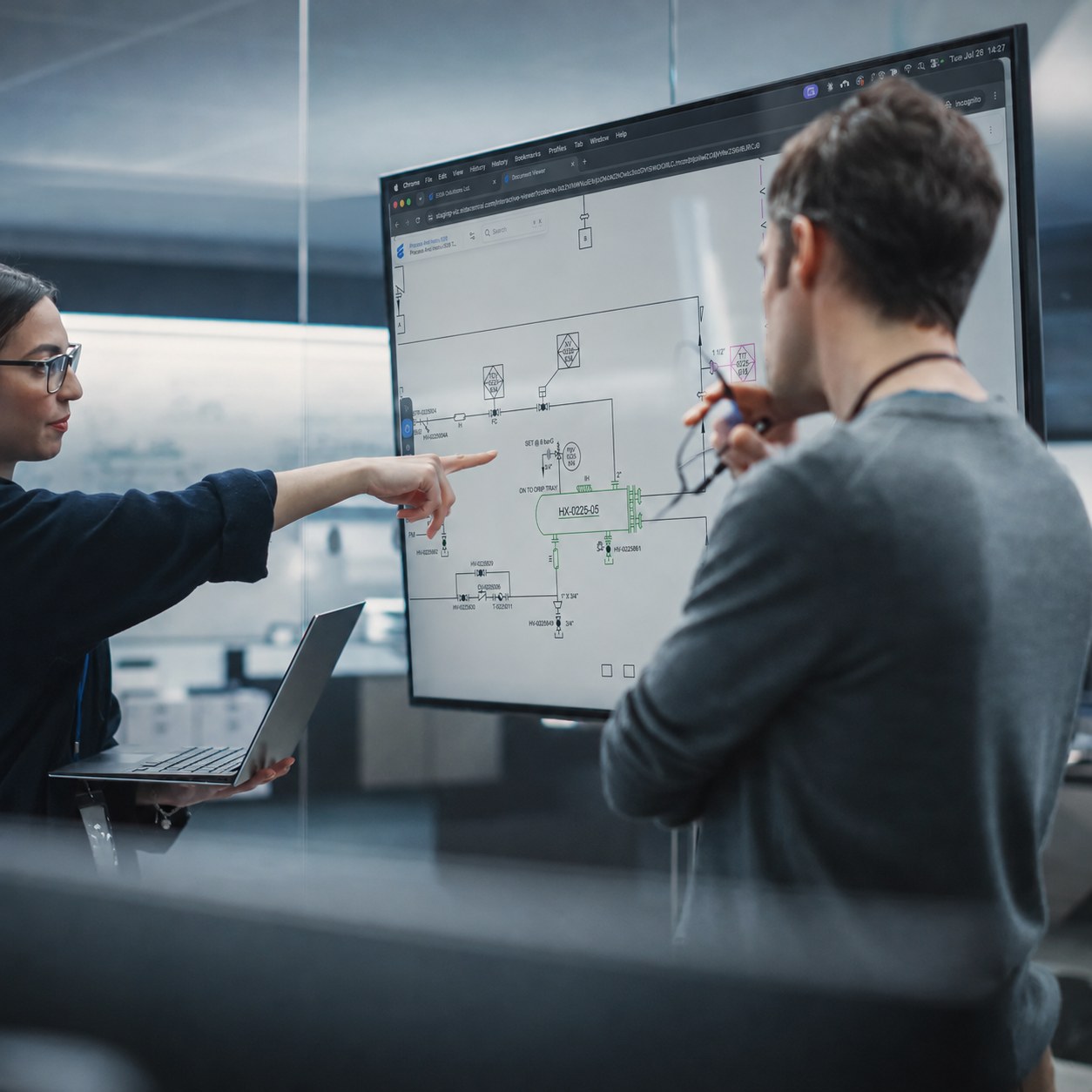 Two engineers reviewing a piping and instrumentation drawing on a large screen